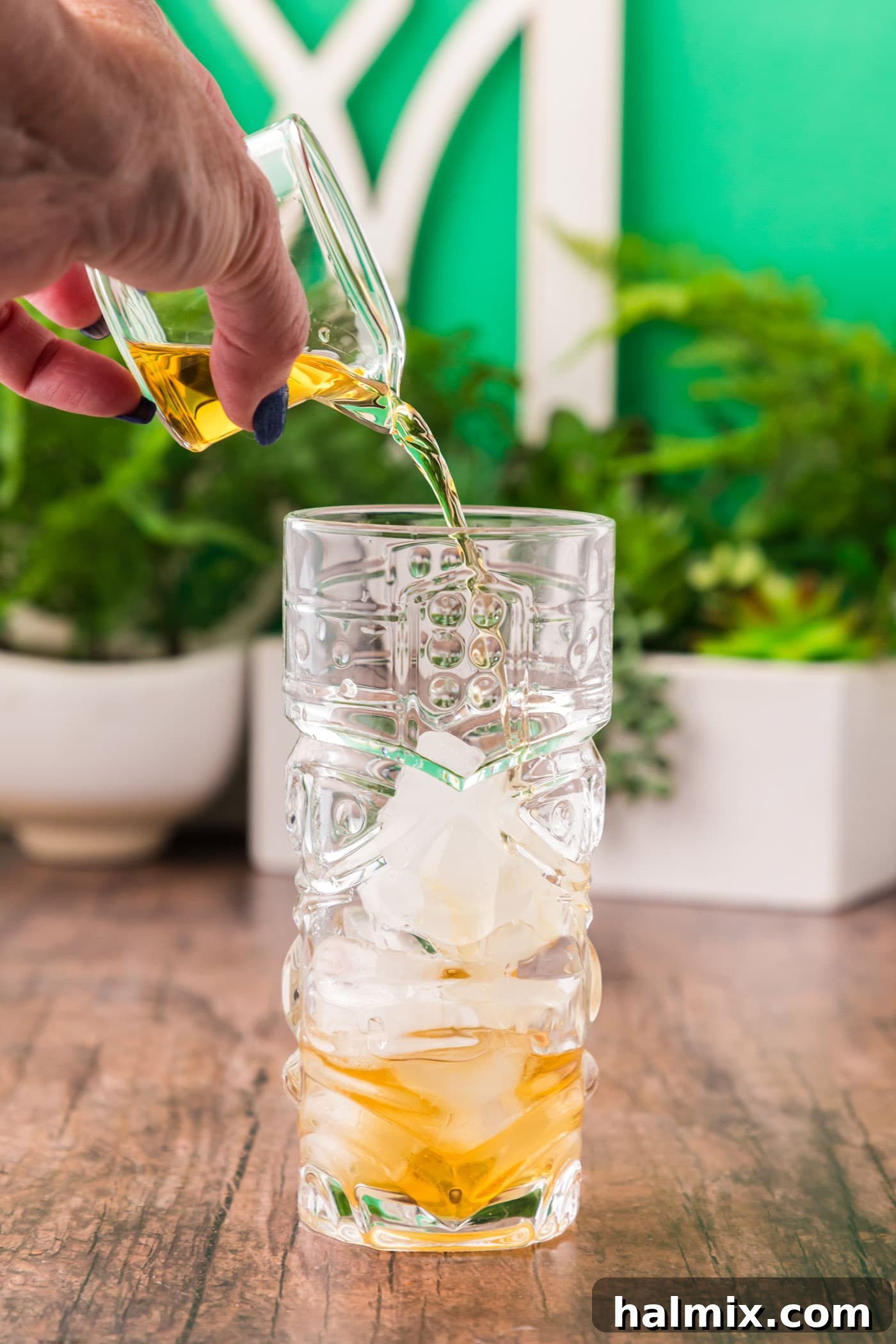 Pouring Jamaican rum into a glass with ice, forming the base of the cocktail.