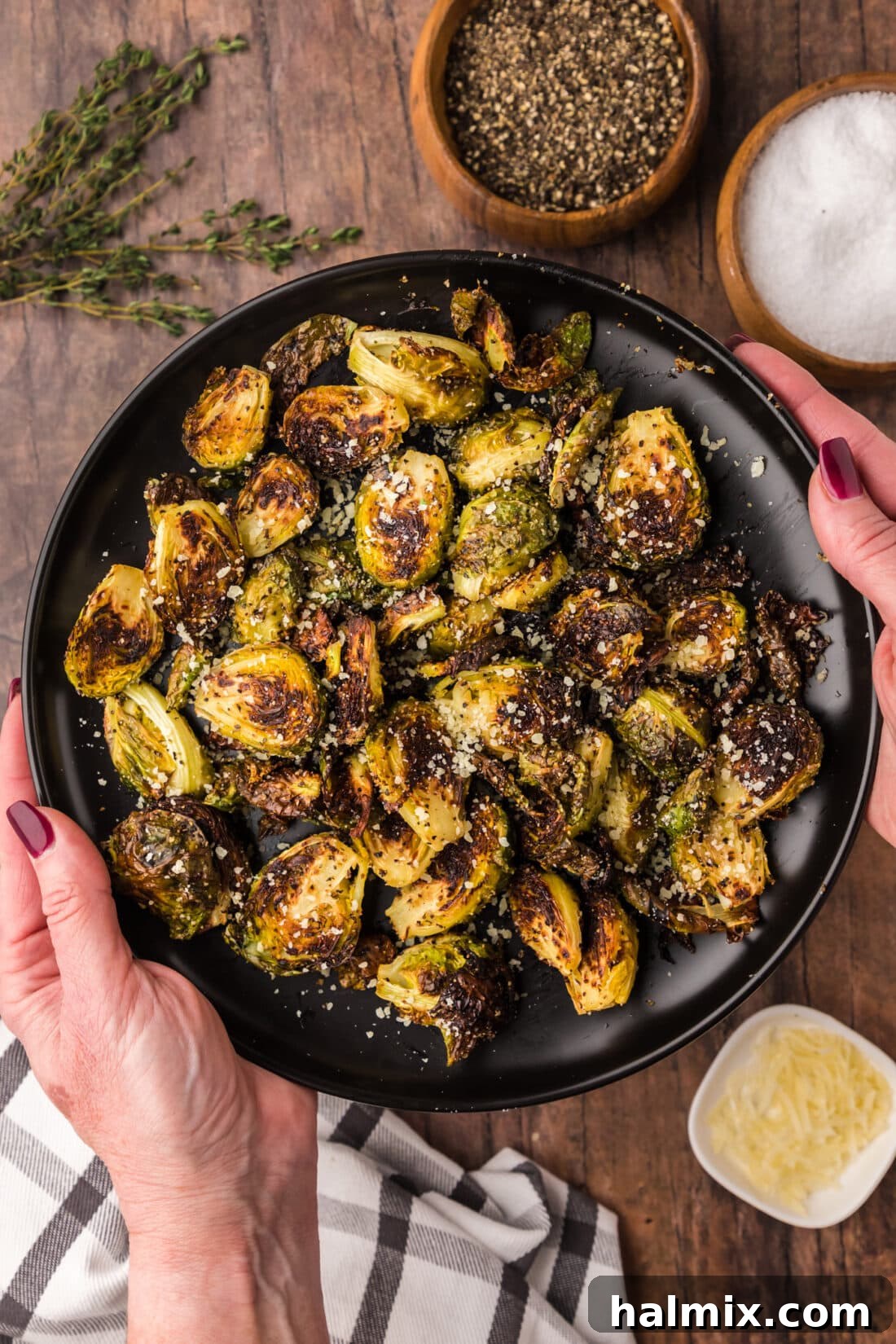 Hands holding a plate of Roasted Brussel Sprouts topped with parmesan