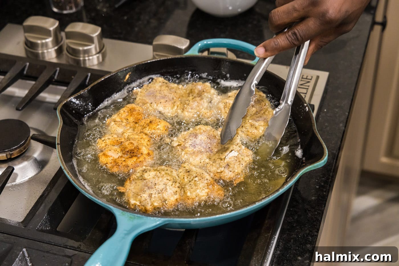 Southern Fried Bliss 14 Tongs flipping a piece of fried chicken in a skillet to cook evenly