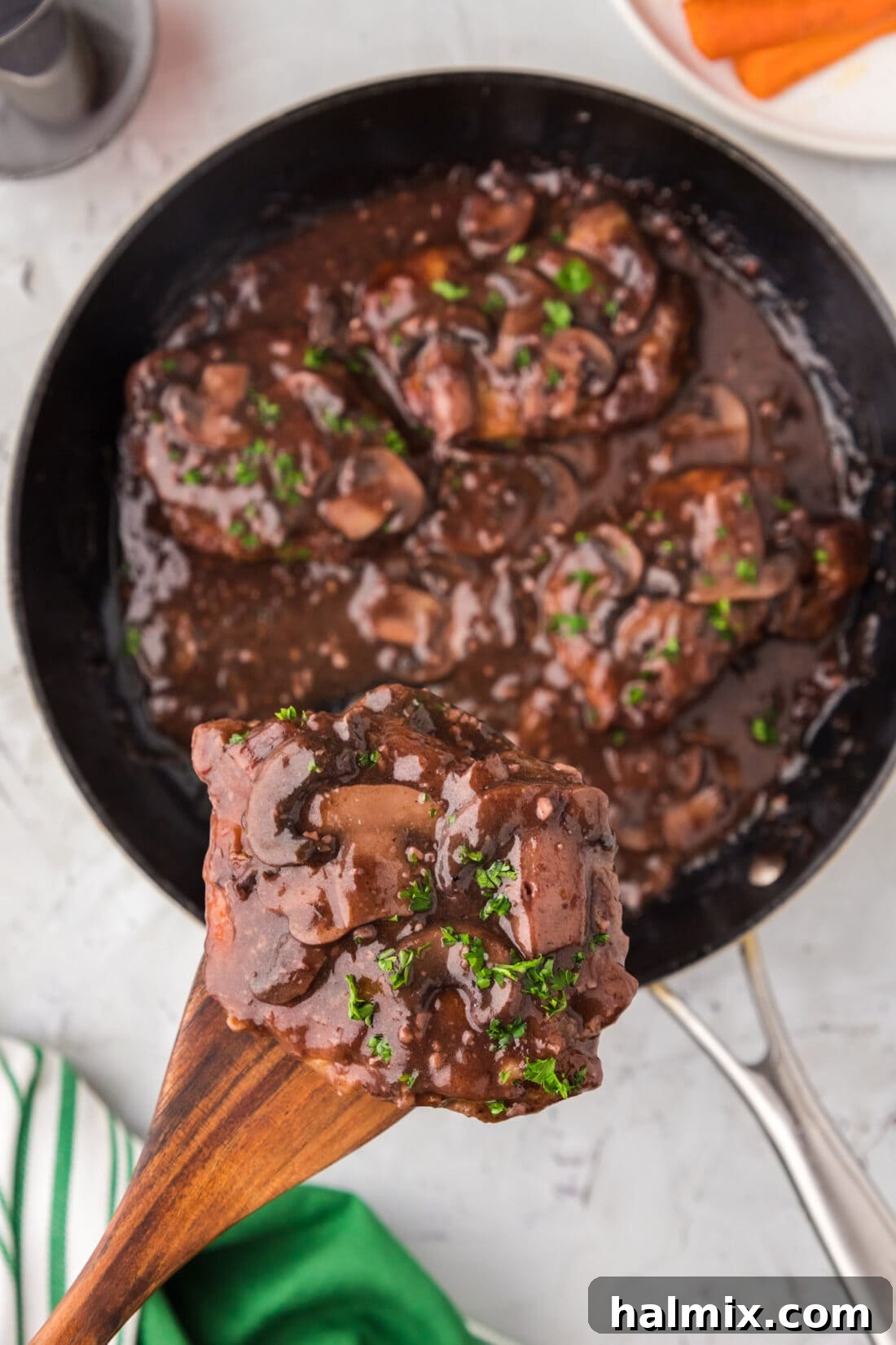 Marsala Veal: Italian Elegance 15 A wooden spatula lifting a succulent piece of Veal Marsala out of a skillet, showcasing the rich mushroom sauce