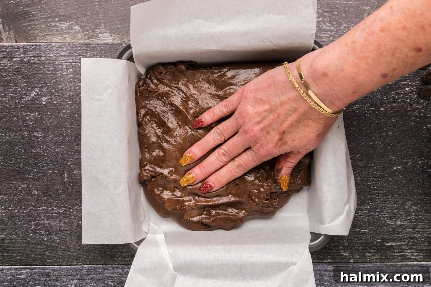 hand pressing down brownie batter in a pan