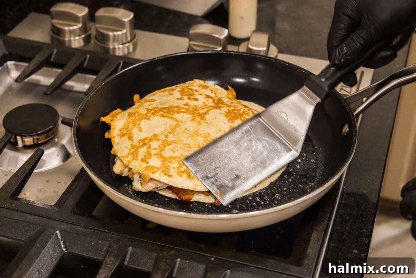 Crispy Ranch Chicken Bacon Quesadillas 17 A fish turner spatula flipping a chicken bacon ranch quesadilla in a skillet to cook the second side.