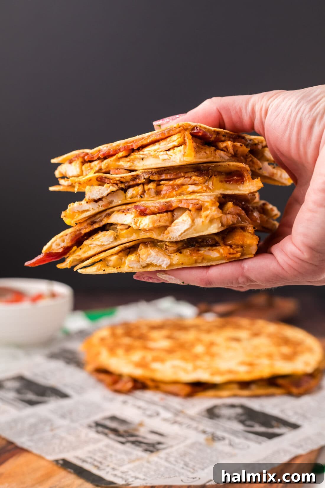 Crispy Ranch Chicken Bacon Quesadillas 3 A hand holds up a single triangular slice of a Chicken Bacon Ranch Quesadilla, showcasing the melted cheese, chicken, and bacon filling.