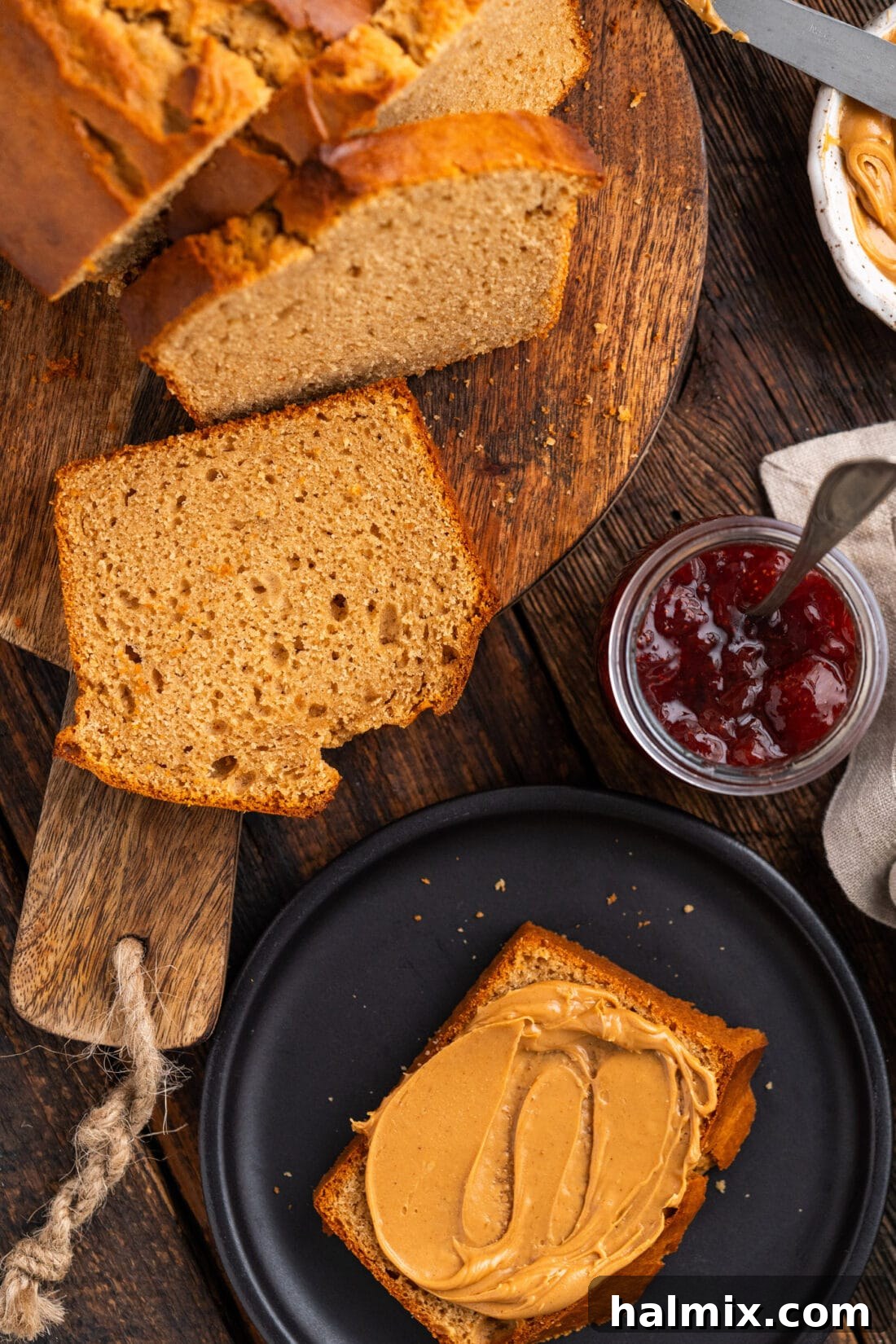 Slices of freshly baked Peanut Butter Bread arranged on a rustic wooden board, with one slice topped with creamy peanut butter.