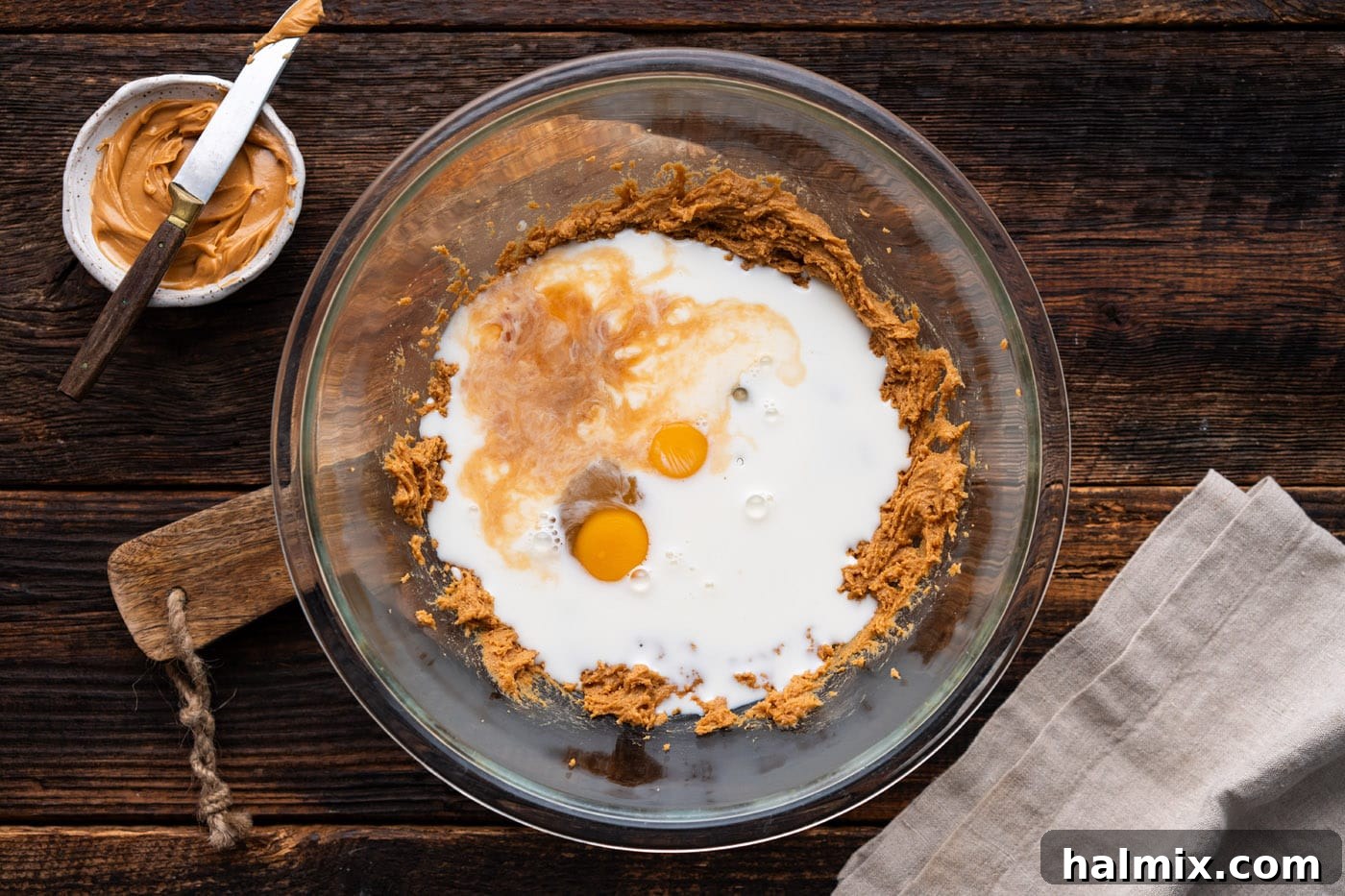 Eggs, milk, and vanilla extract being added to the creamy peanut butter mixture in a bowl.