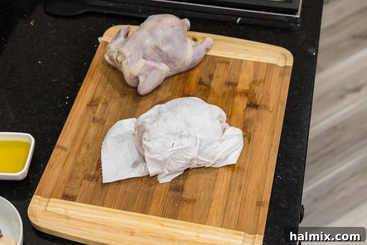 Patting Cornish hens dry with paper towels on a wooden cutting board to remove excess moisture.