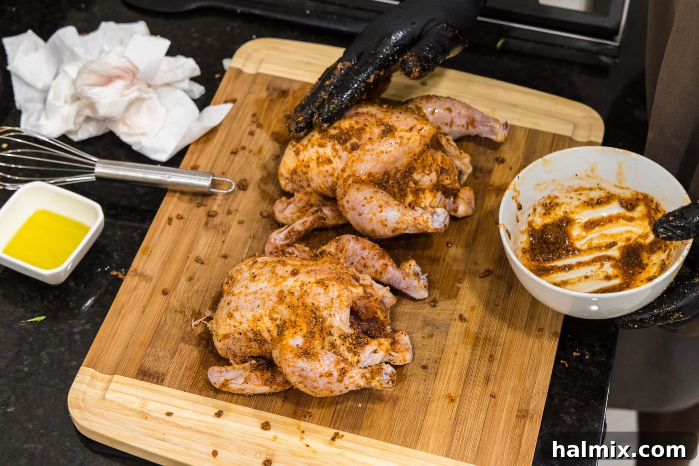 A gloved hand meticulously rubbing seasoning paste onto a Cornish hen, ensuring full coverage.