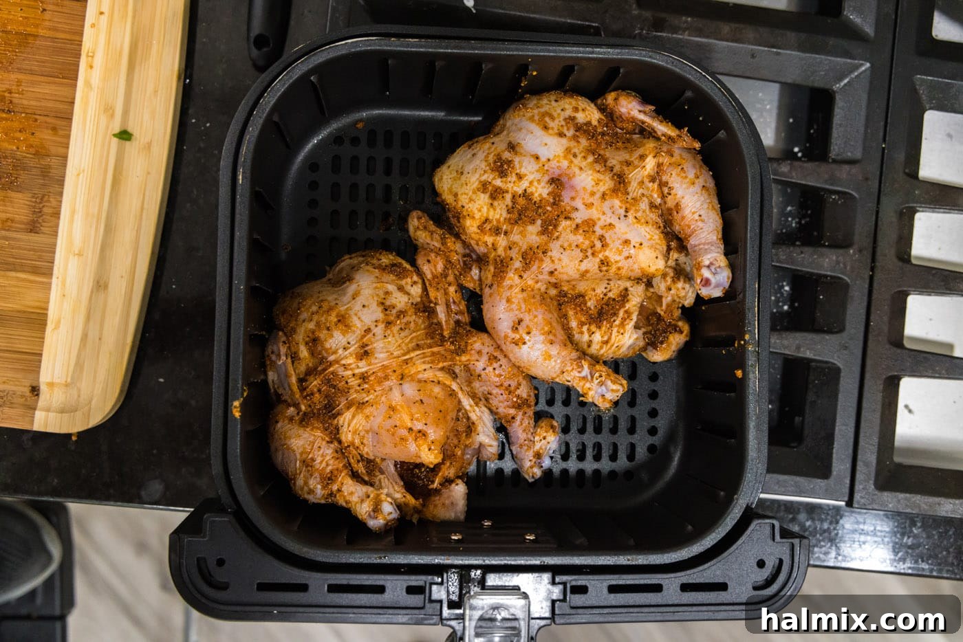 Two Cornish hens cooking breast-side up in an air fryer basket, with ample space for air circulation.