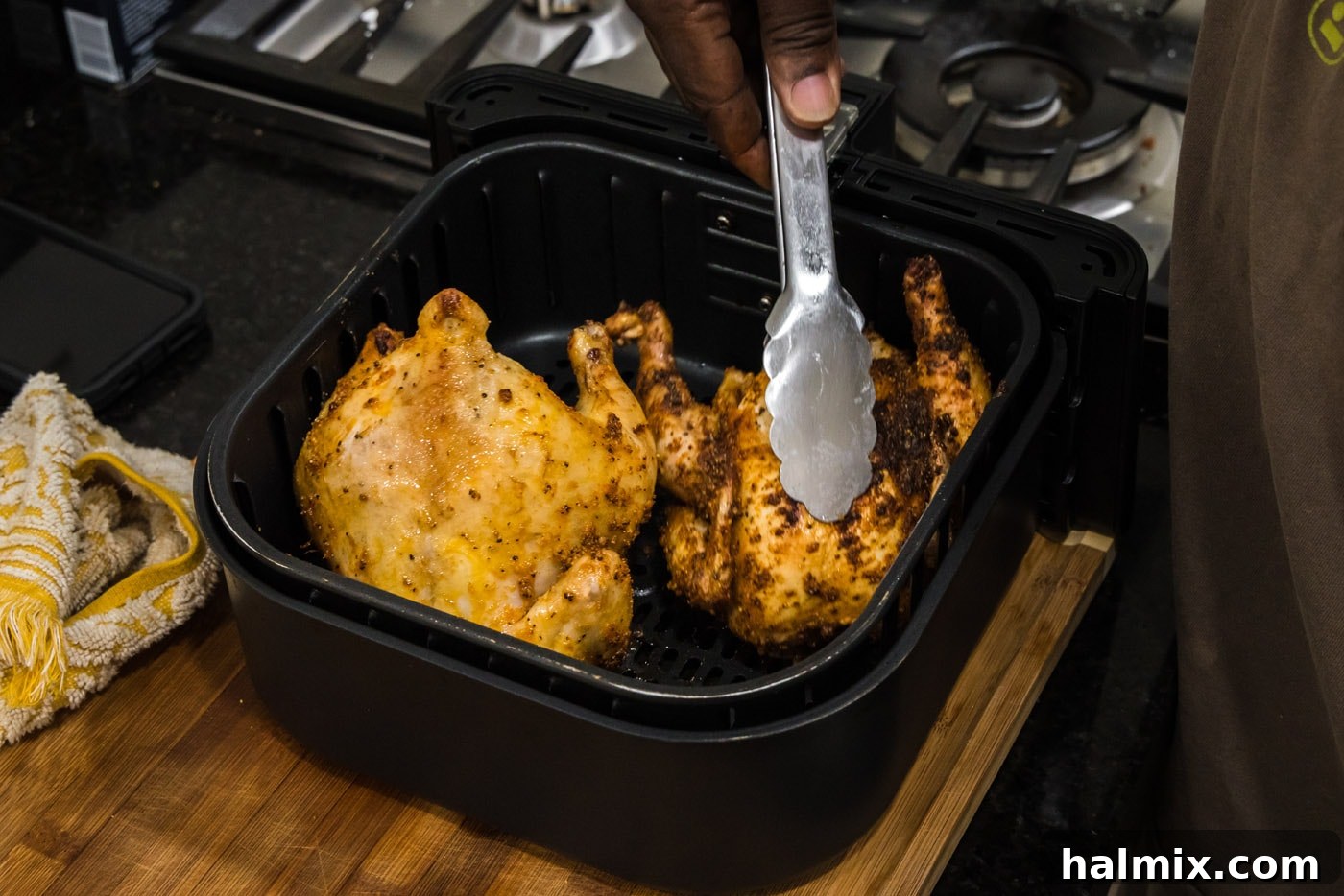 Tongs flipping Cornish hens over in an air fryer basket for even cooking and browning.