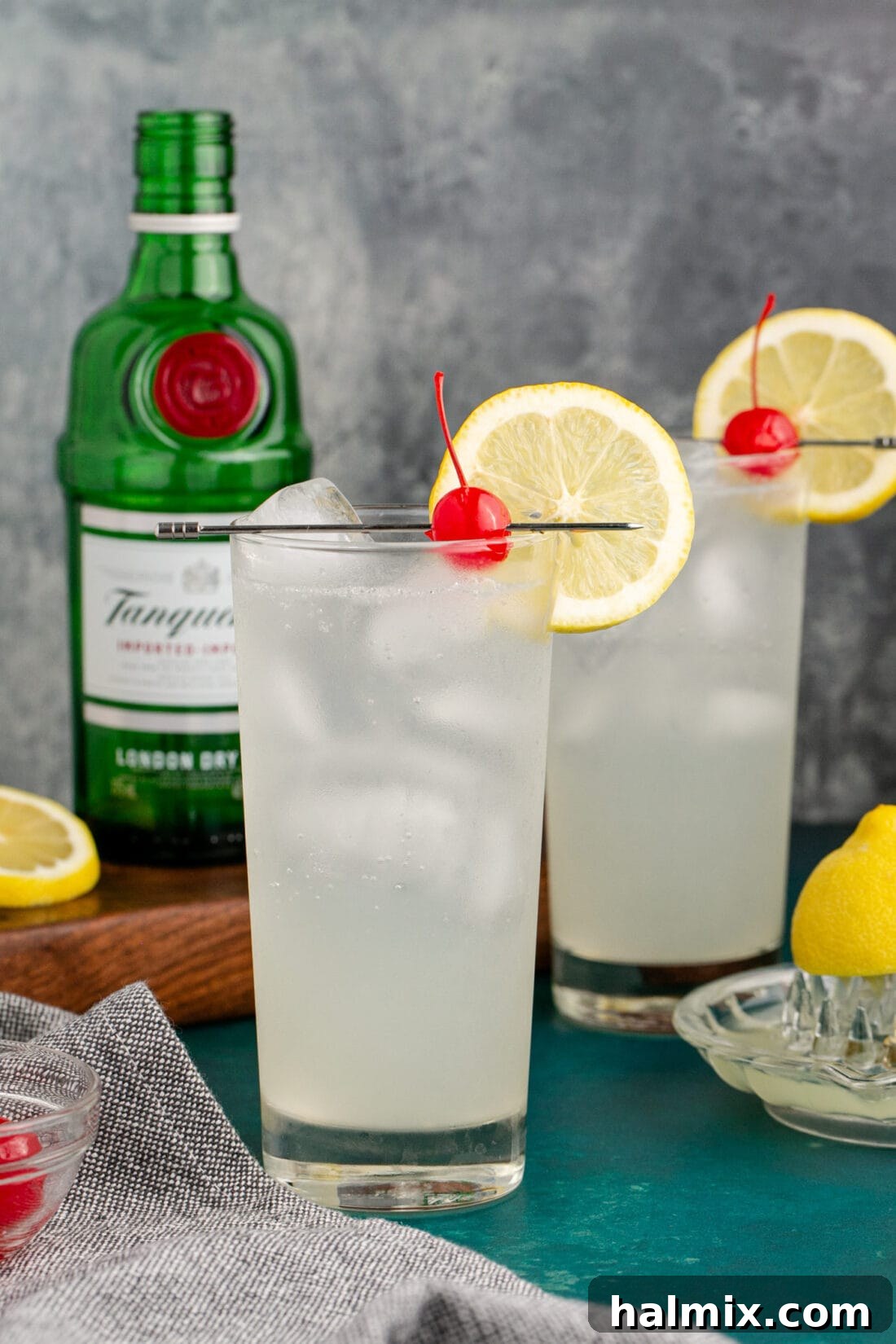 Two Tom Collins cocktails with a bottle of gin in the background