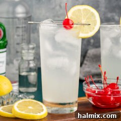 Tom Collins cocktail on a wooden board with lemon wheels and cherries on the side for garnish