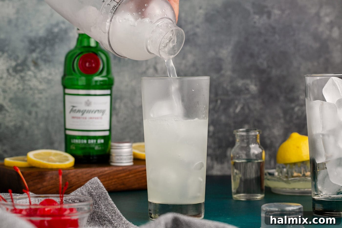 straining tom collins cocktail into a glass of ice
