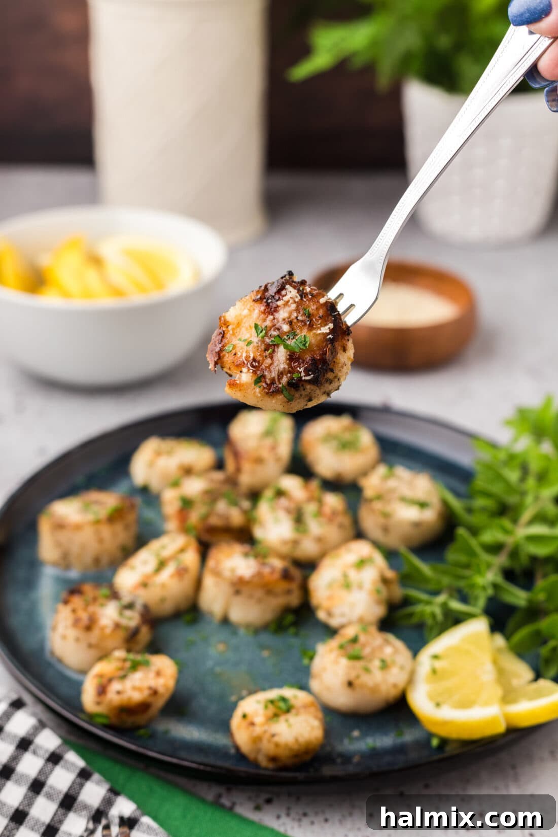 A perfectly grilled scallop on a seafood fork, held above a plate of other grilled scallops