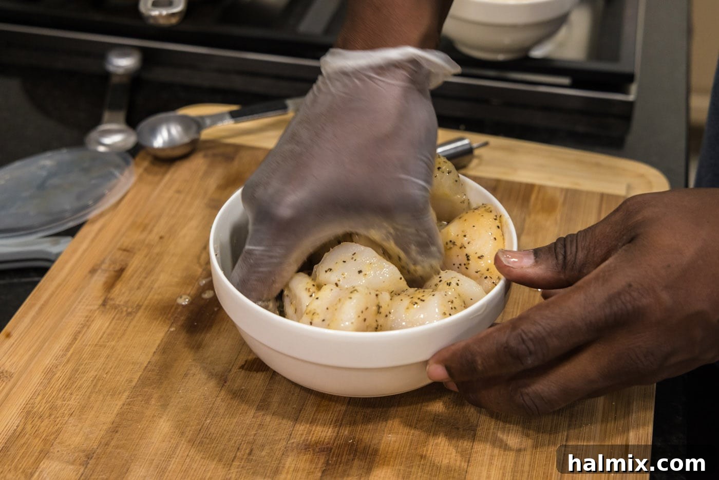 Gloved hand mixing scallops with the butter mixture in a bowl