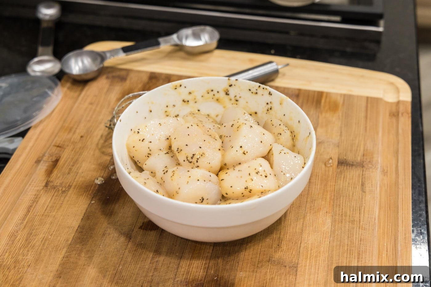 Scallops in a bowl, fully coated with the butter and seasoning mixture