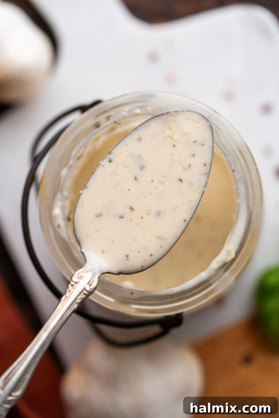 A spoon dripping with creamy Garlic Parmesan Wing Sauce above a jar