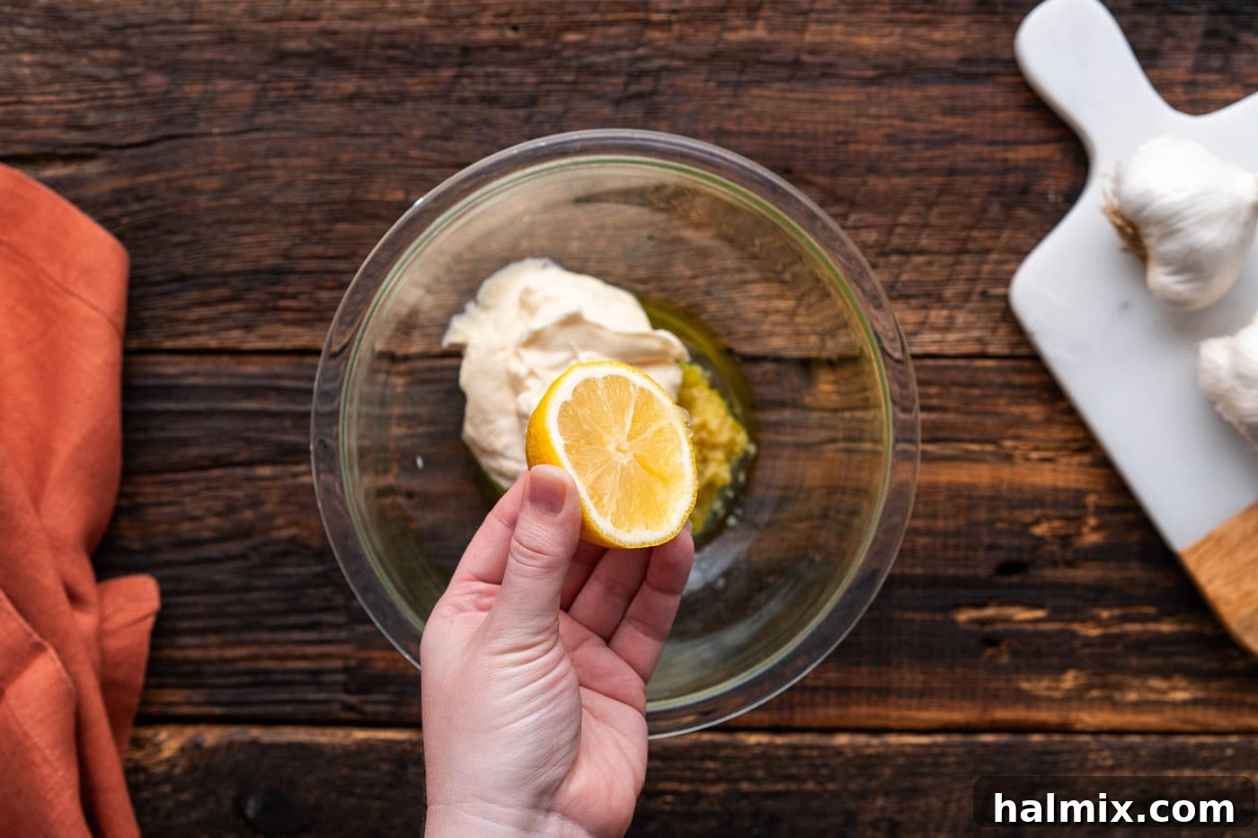 Squeezing fresh lemon juice into a bowl with garlic parmesan wing sauce ingredients