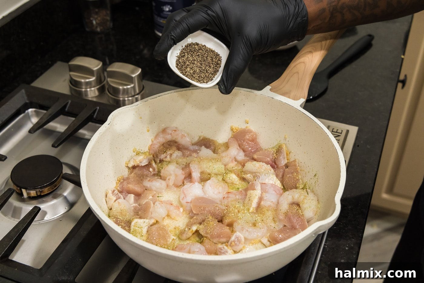 Creamy Chicken and Shrimp Carbonara 6 Hand adding seasoning, likely garlic salt and black pepper, to the chicken and shrimp mixture in the skillet.