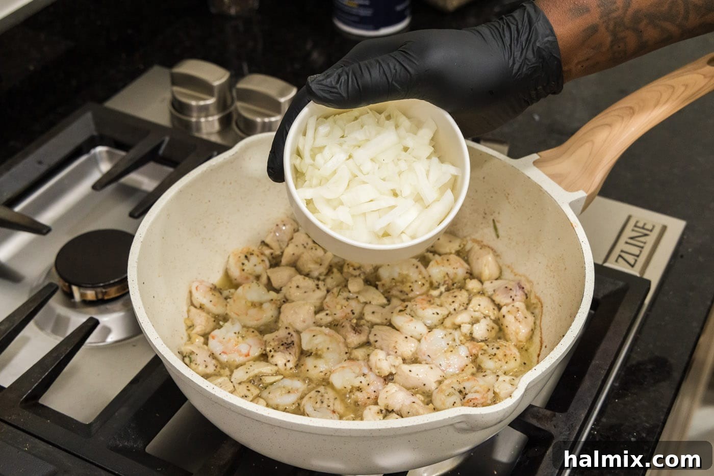 Creamy Chicken and Shrimp Carbonara 7 Hand adding chopped onion to the skillet containing cooked chicken and shrimp.