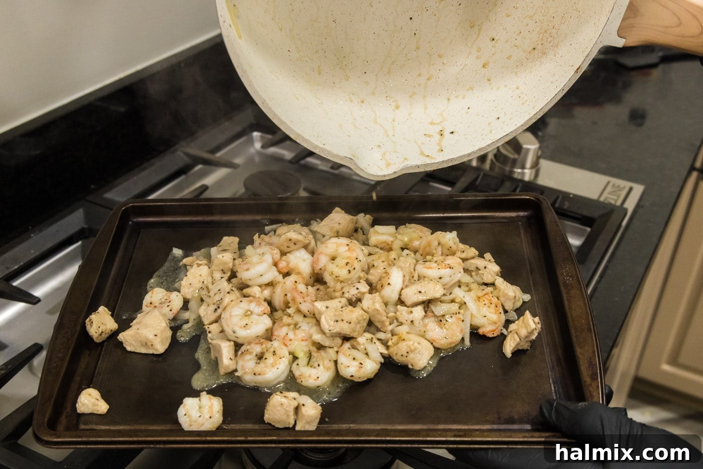Creamy Chicken and Shrimp Carbonara 8 Cooked chicken, shrimp, and onion mixture being poured from the skillet onto a baking sheet to rest.