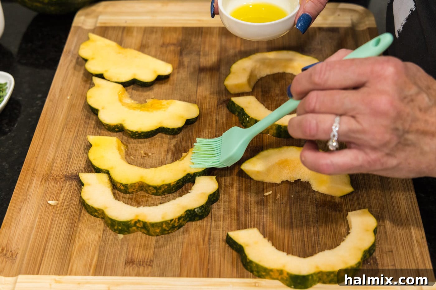 Basting acorn squash slices generously with olive oil using a brush before seasoning.