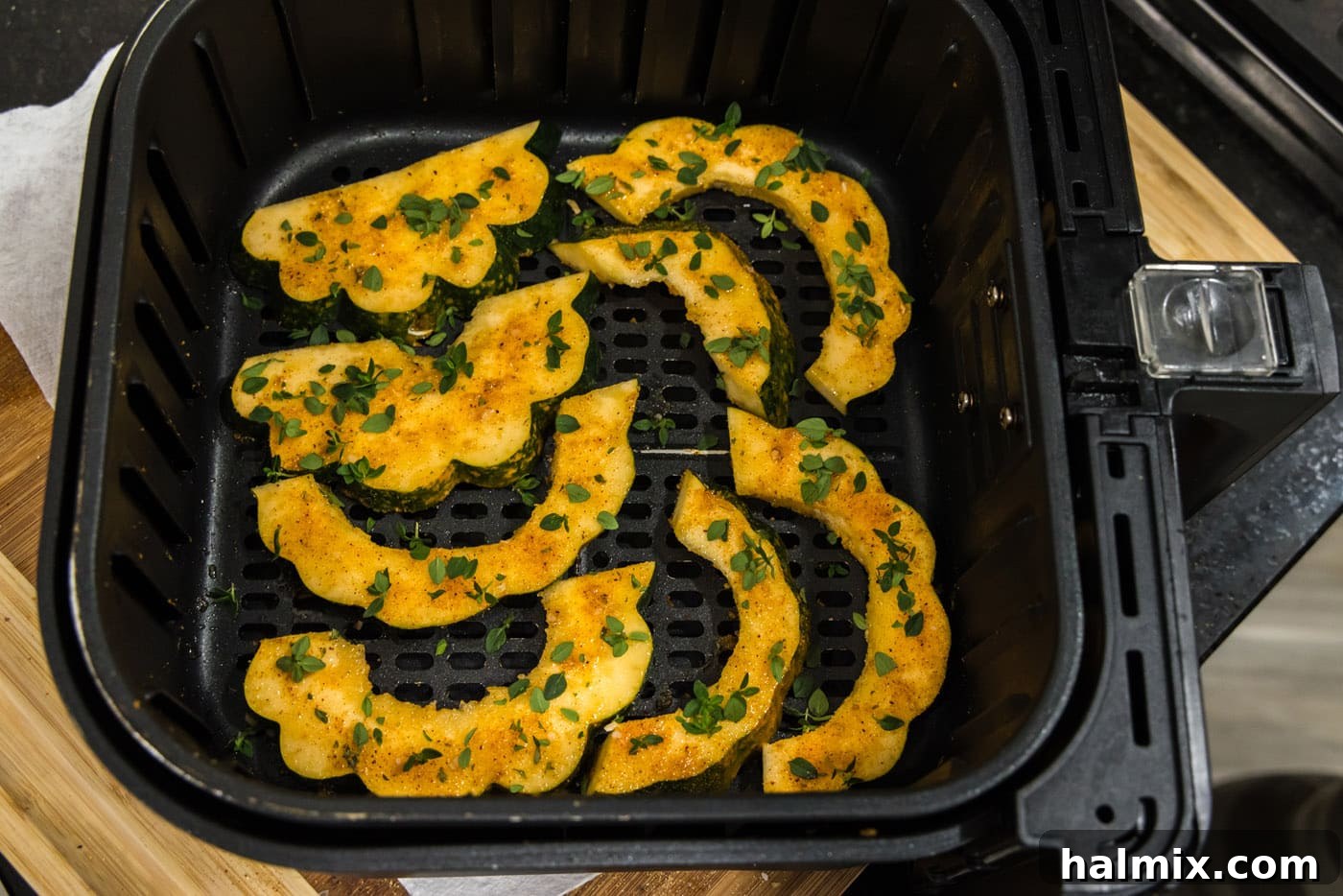 Fresh thyme leaves being sprinkled over acorn squash slices in the air fryer for added aroma.