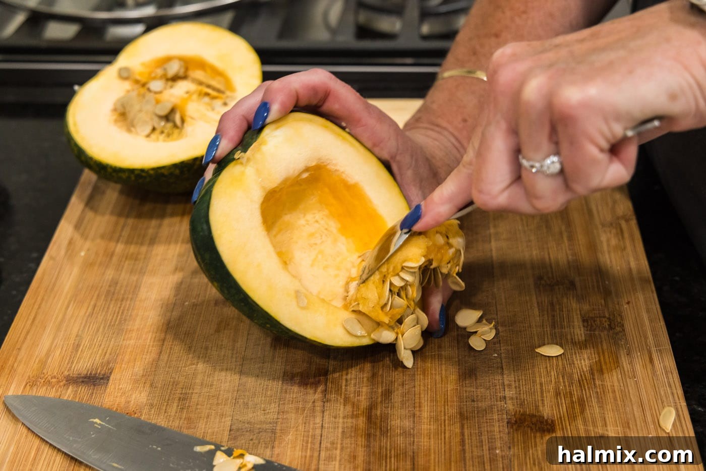 Scooping out the seeds and fibrous pulp from a halved acorn squash with a spoon.