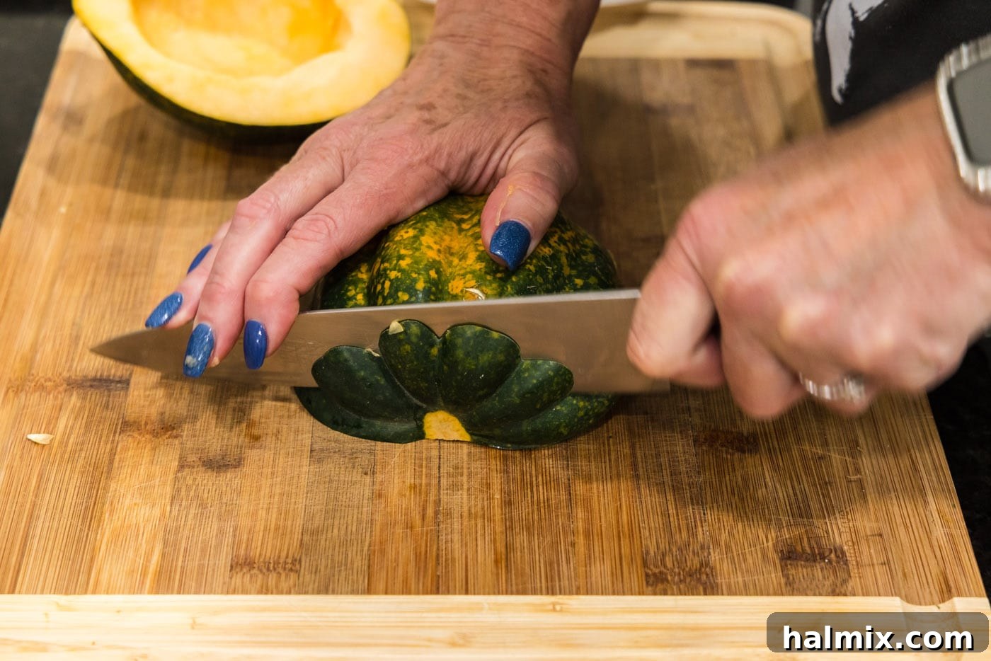 Slicing an acorn squash on a cutting board into consistent 3/4-inch pieces.