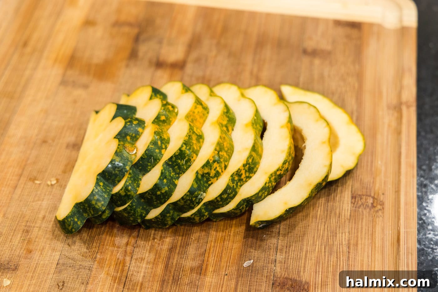 Neatly arranged, uniformly sliced acorn squash pieces on a cutting board, ready for seasoning.