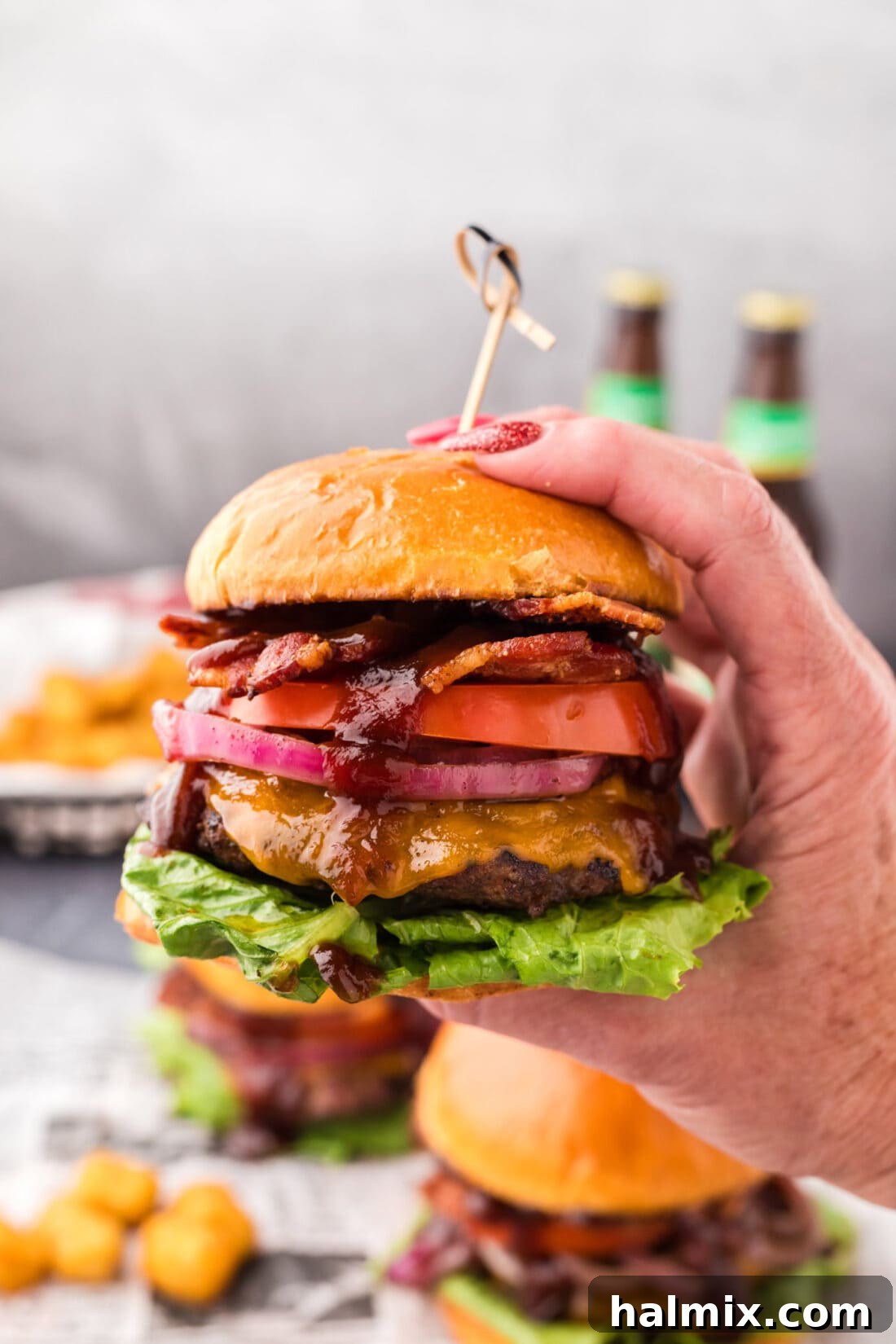 Hand holding up a BBQ Bacon Burger, showing off its generous layers of cheese, bacon, and caramelized onions.