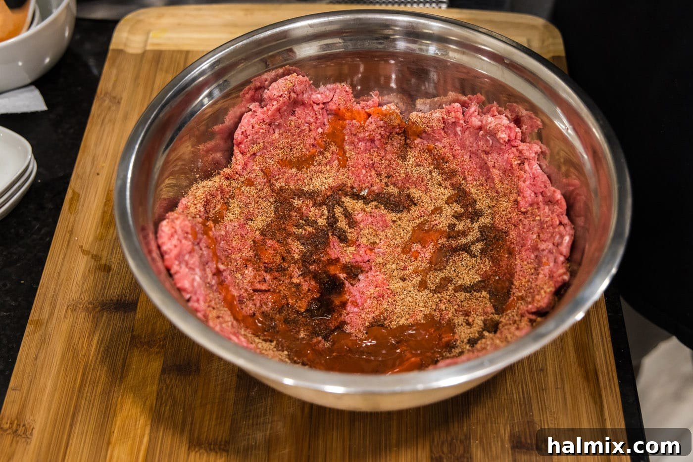 mixing burger meat with seasonings in a bowl, demonstrating the even distribution of spices.