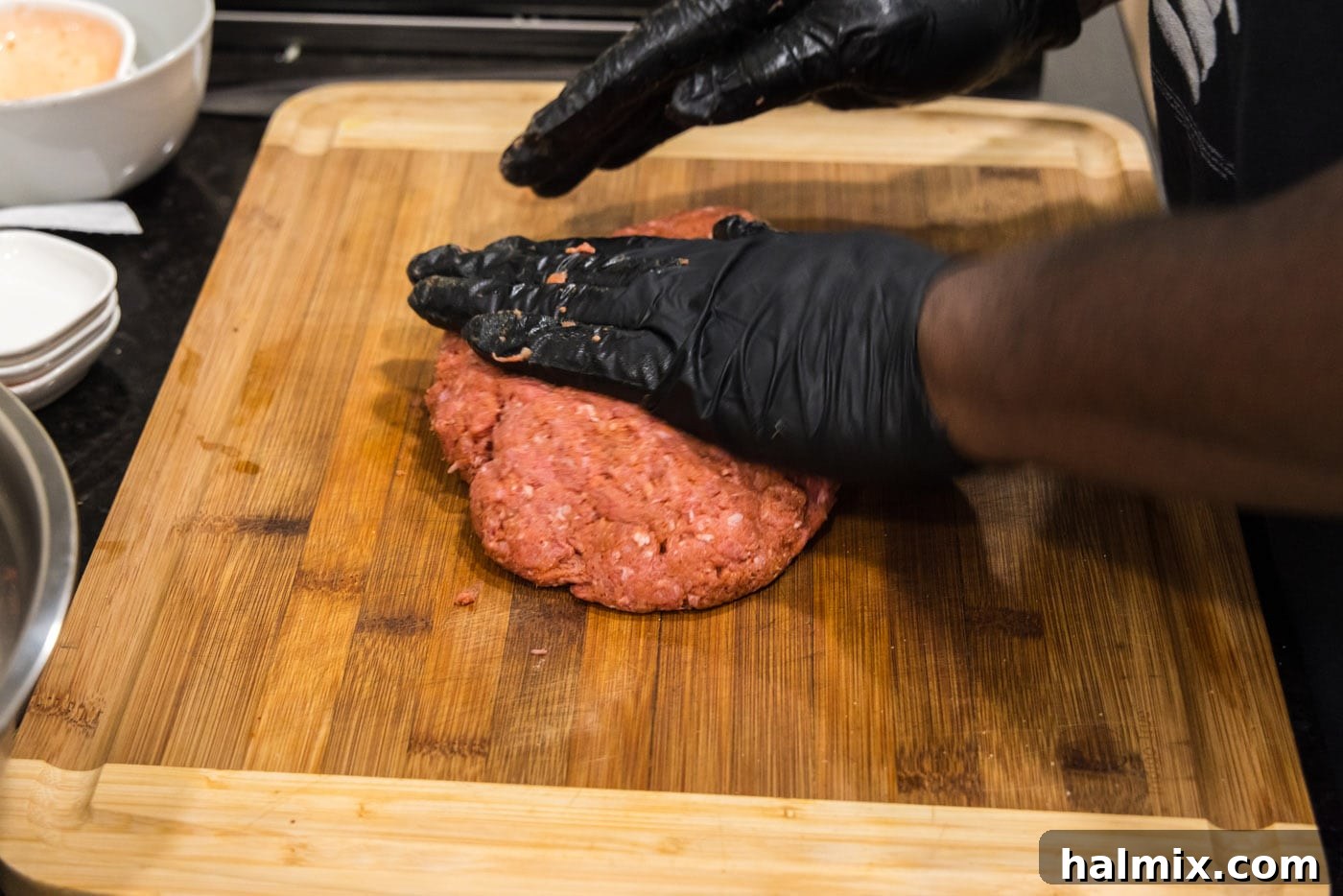 hands flattening burger meat on a cutting board, preparing patties for grilling.