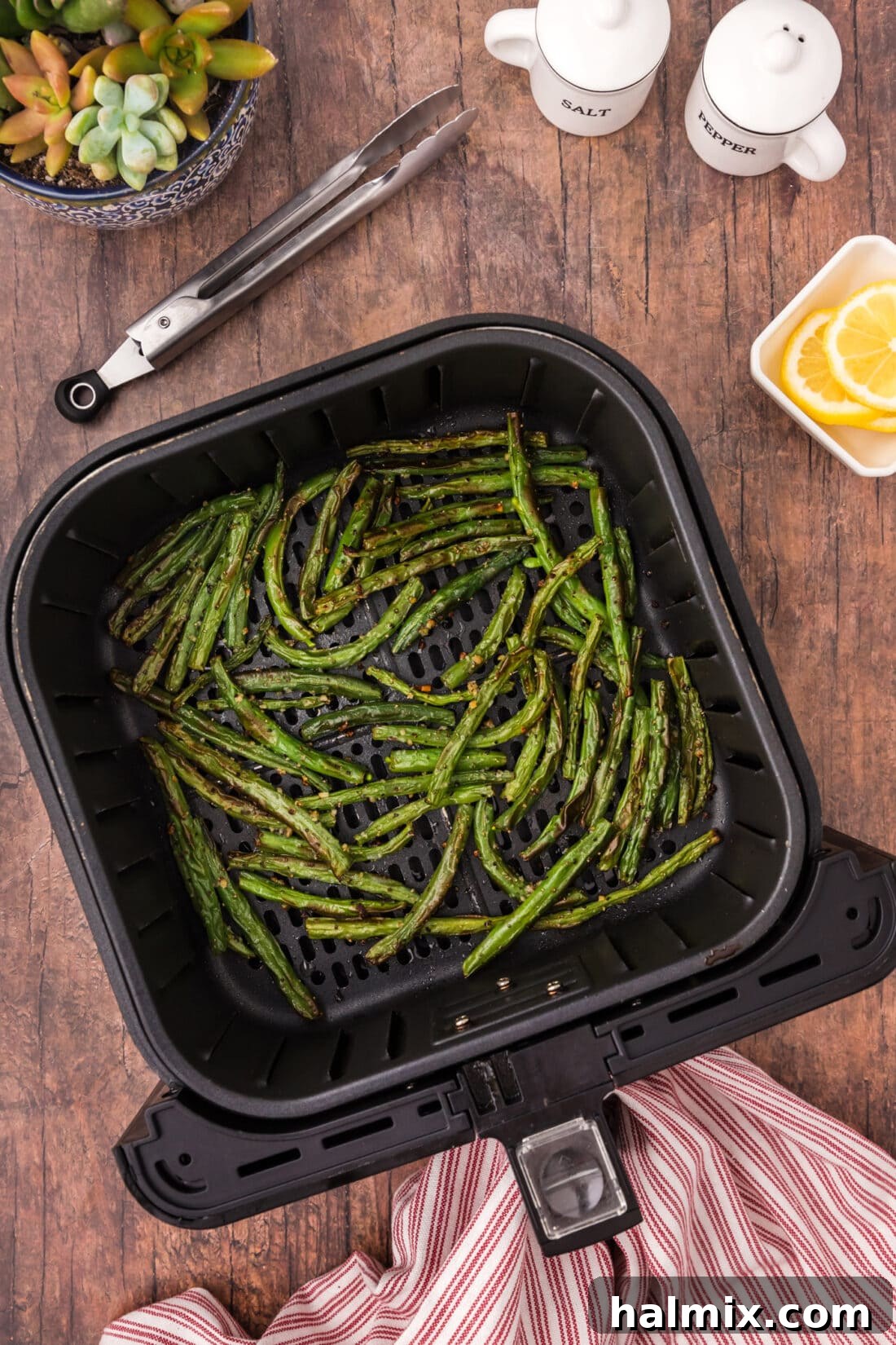 Freshly seasoned green beans waiting in an air fryer basket before the cooking process begins.