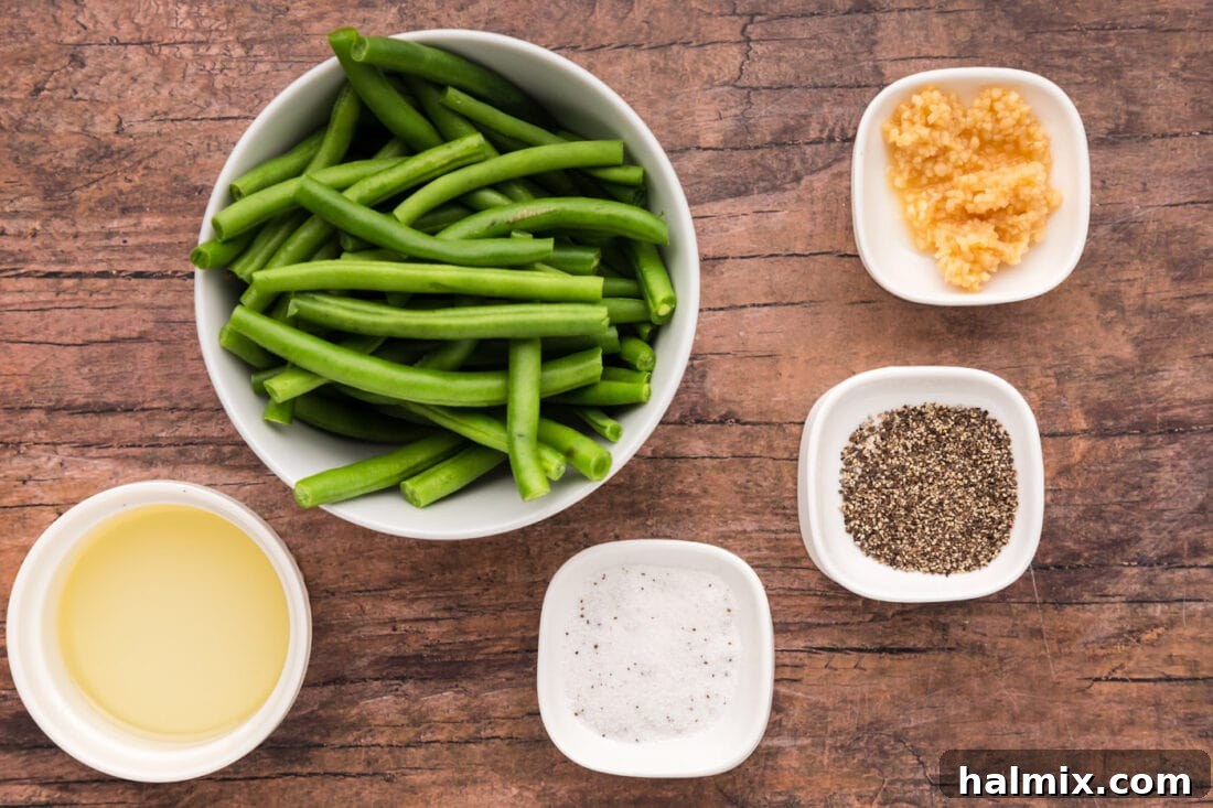 A collection of the 5 essential ingredients for air fryer green beans: fresh green beans, minced garlic, salt, black pepper, and olive oil, laid out on a wooden surface.