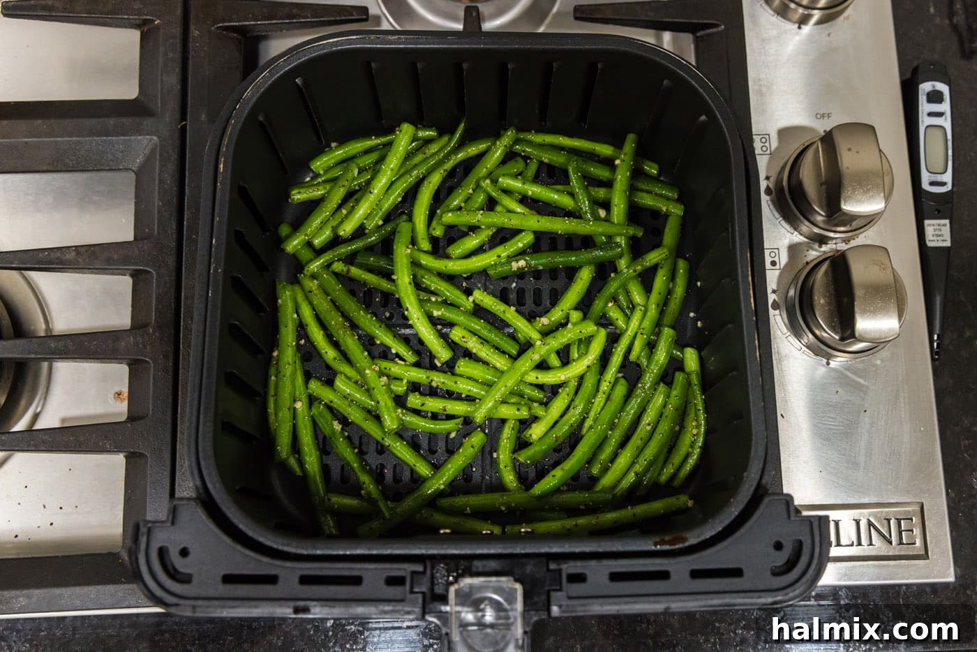 Fresh green beans, coated with garlic and seasonings, arranged neatly in a single layer in the air fryer basket, ready for cooking.