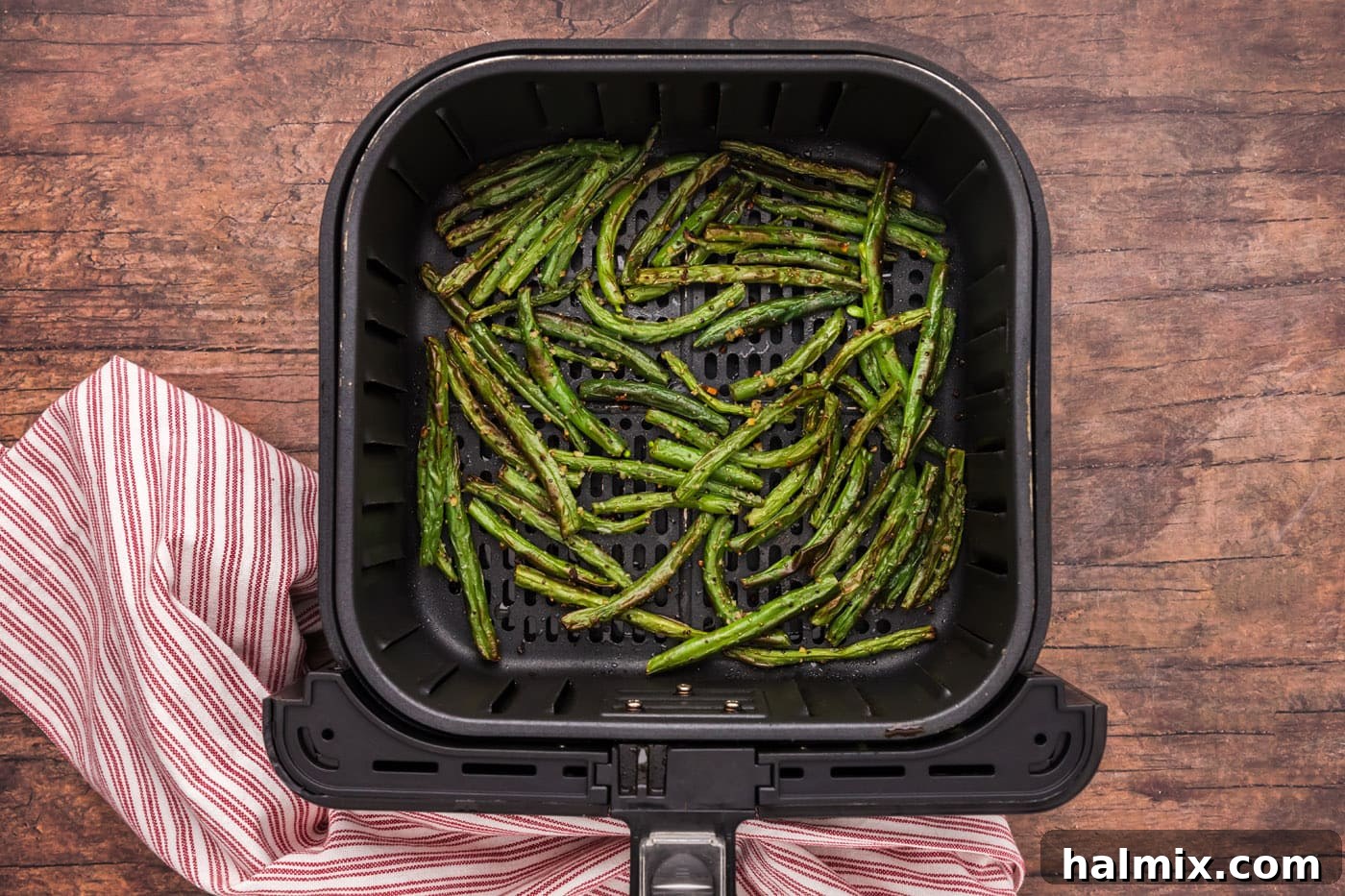 Air fryer green beans cooking in the basket, showing a developing golden-brown char after being shaken halfway through.