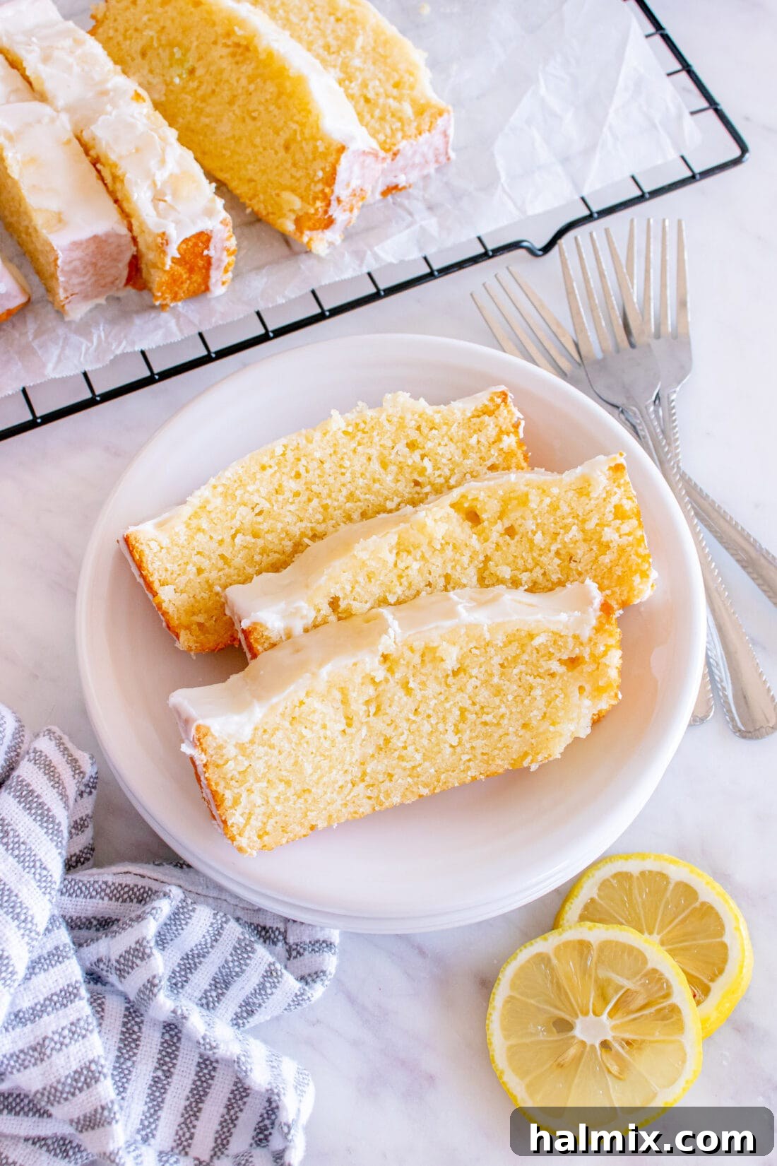Three slices of Lemon Pound Cake on a plate with more slices in the background, showcasing its tender crumb and glistening lemon glaze.