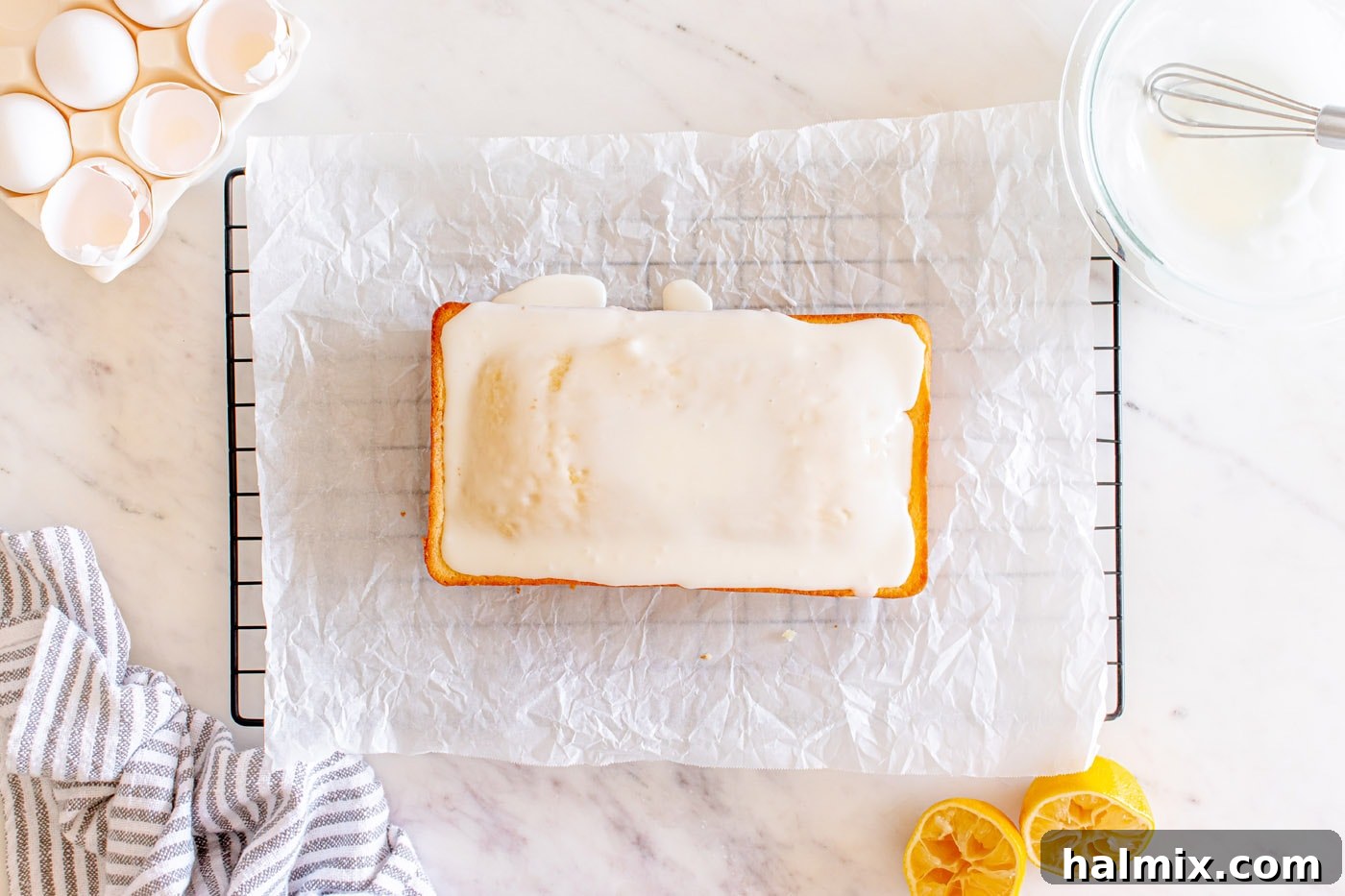 Iced lemon pound cake on parchment paper with glaze beautifully dripped down the sides.