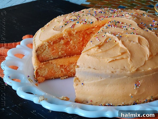 A top-down view of the Orange Poke Cake, showing its creamy frosting and a hint of the orange color beneath, enticing viewers to try a slice.