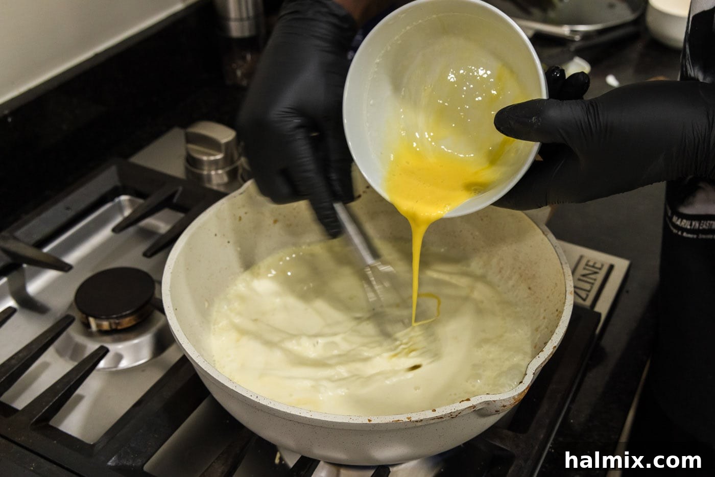 Slowly drizzling whisked eggs into the heavy cream in a skillet while continuously whisking to temper them and create a smooth carbonara sauce.