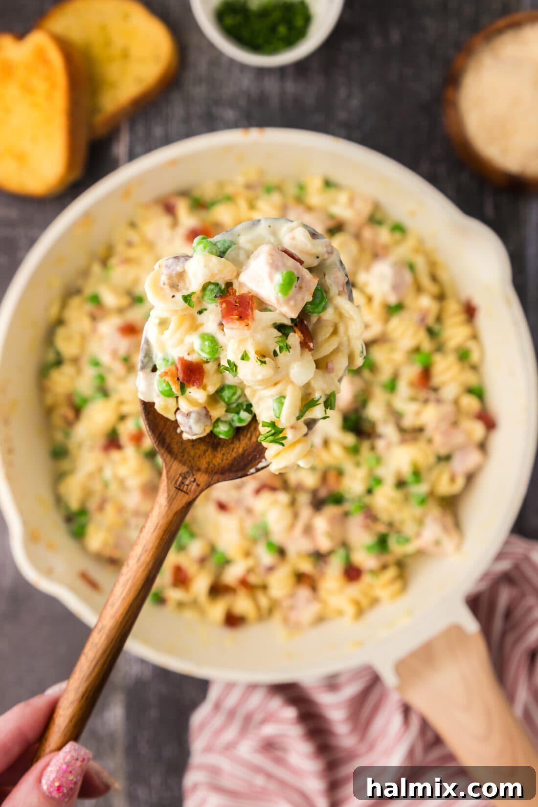 A serving spoon lifting a generous portion of Turkey Carbonara from a skillet, showing the rich, creamy sauce and all the components ready to be savored.