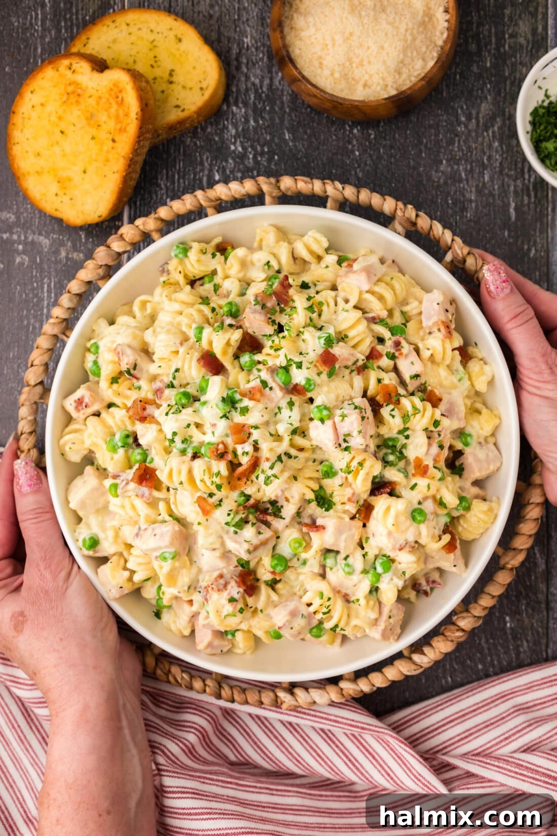 A pair of hands gently holding a rustic serving bowl filled with steaming Turkey Carbonara, highlighting the rich texture and vibrant ingredients.