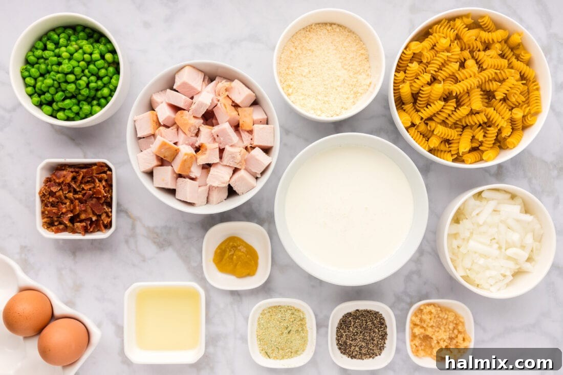 A flat lay photograph displaying all the fresh ingredients needed for Turkey Carbonara, including pasta, cubed turkey, bacon, peas, onion, garlic, olive oil, heavy cream, eggs, and parmesan cheese.
