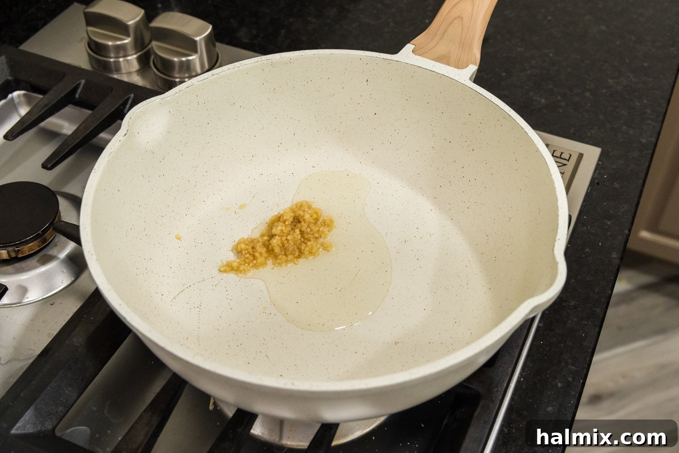 Minced garlic sizzling in olive oil in a large deep-sided skillet, releasing its fragrant aroma as it begins to soften.