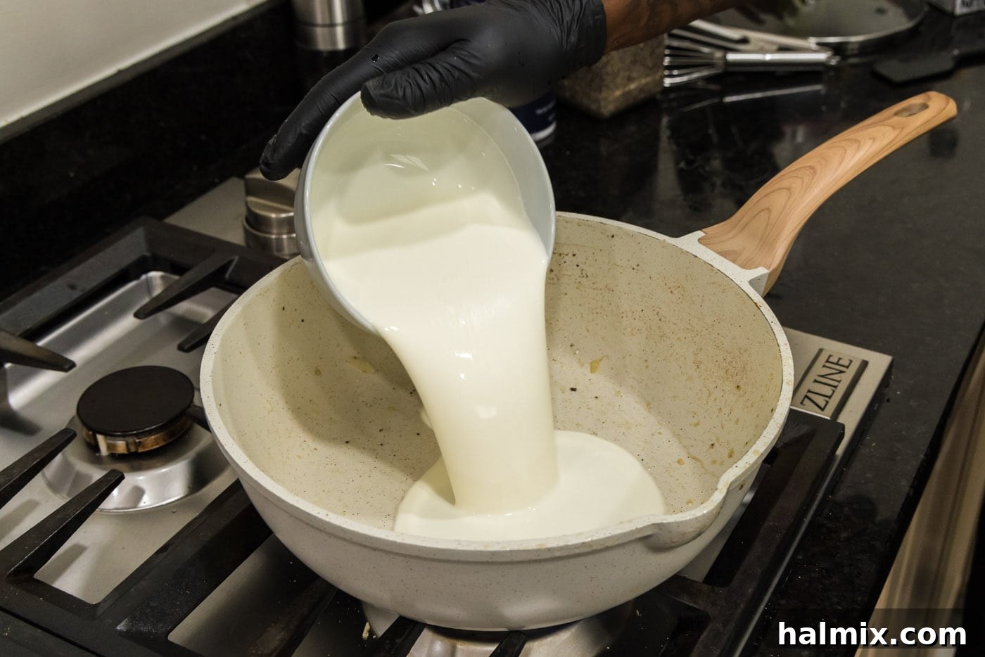 Heavy whipping cream being poured directly into the hot skillet, forming the creamy base for the carbonara sauce.
