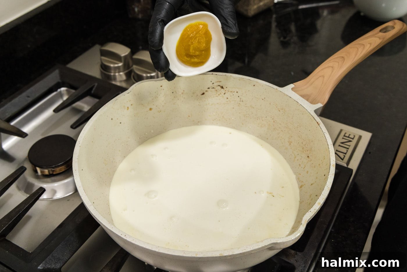 Adding chicken base to the heavy cream in the skillet, ready to be whisked for a richer flavor.
