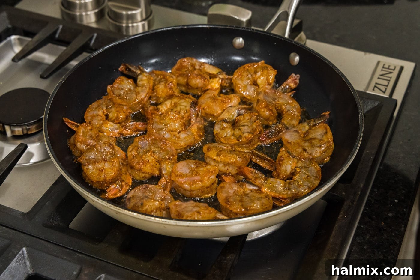 Seasoned shrimp cooking in a hot skillet, showing the beginning of the searing process.