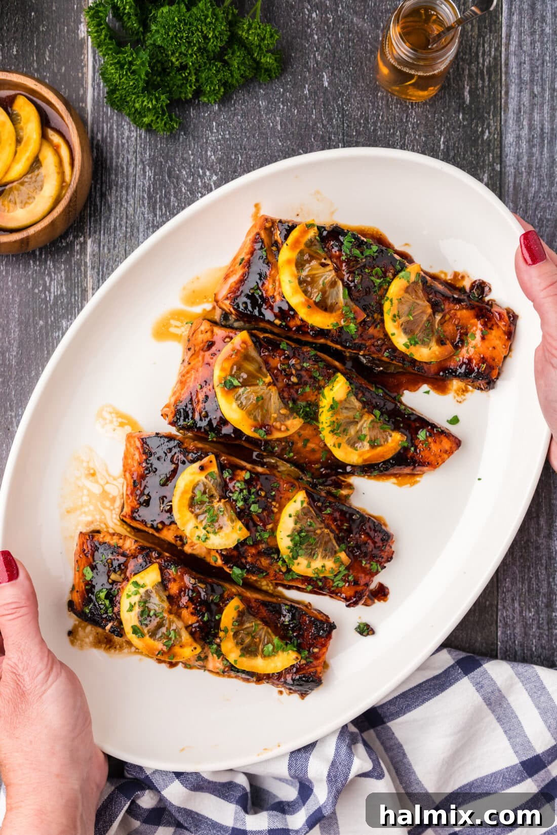 Hands holding a platter of freshly cooked Honey Salmon, garnished beautifully.