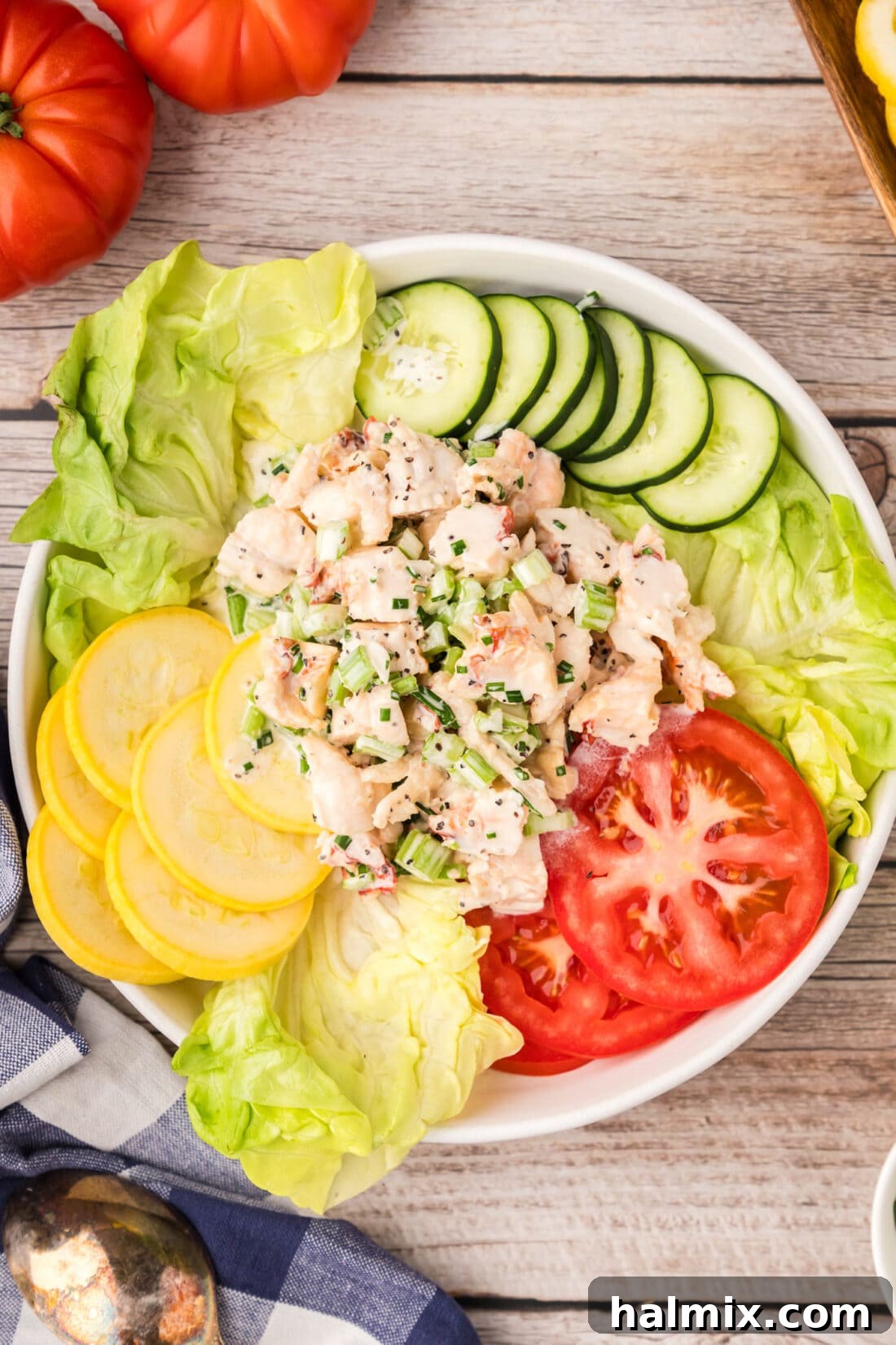 A vibrant bowl of freshly prepared lobster salad, garnished with a sprig of fresh herbs, ready to be served alongside crisp greens and other vegetables.