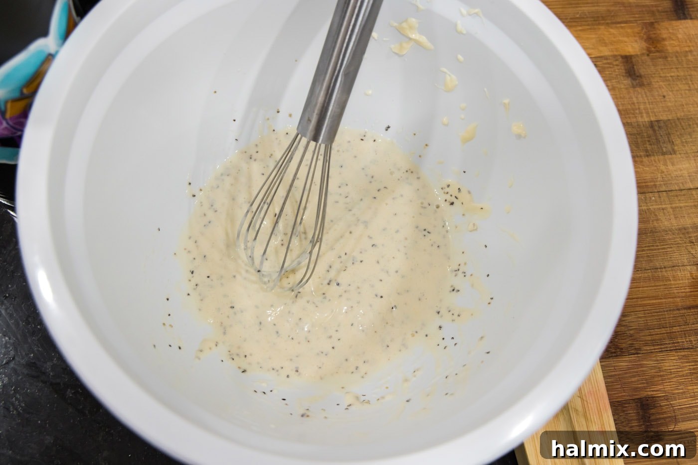 A hand whisking the mayonnaise-based dressing ingredients vigorously in a bowl, showing a smooth, creamy consistency forming.